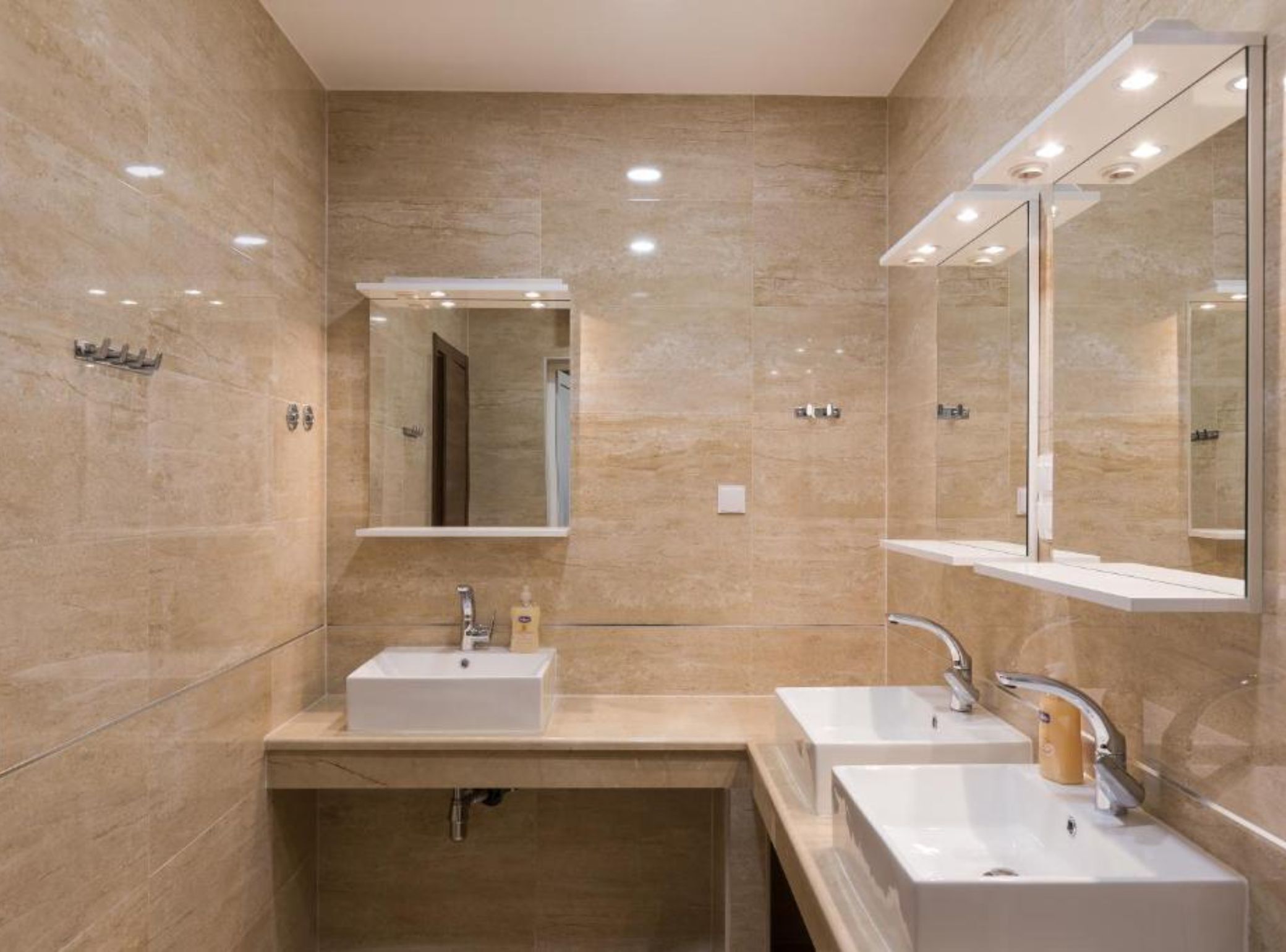 Ein modernes Badezimmer mit zwei Waschbecken, einem großen Spiegel und Einbaustrahlern.