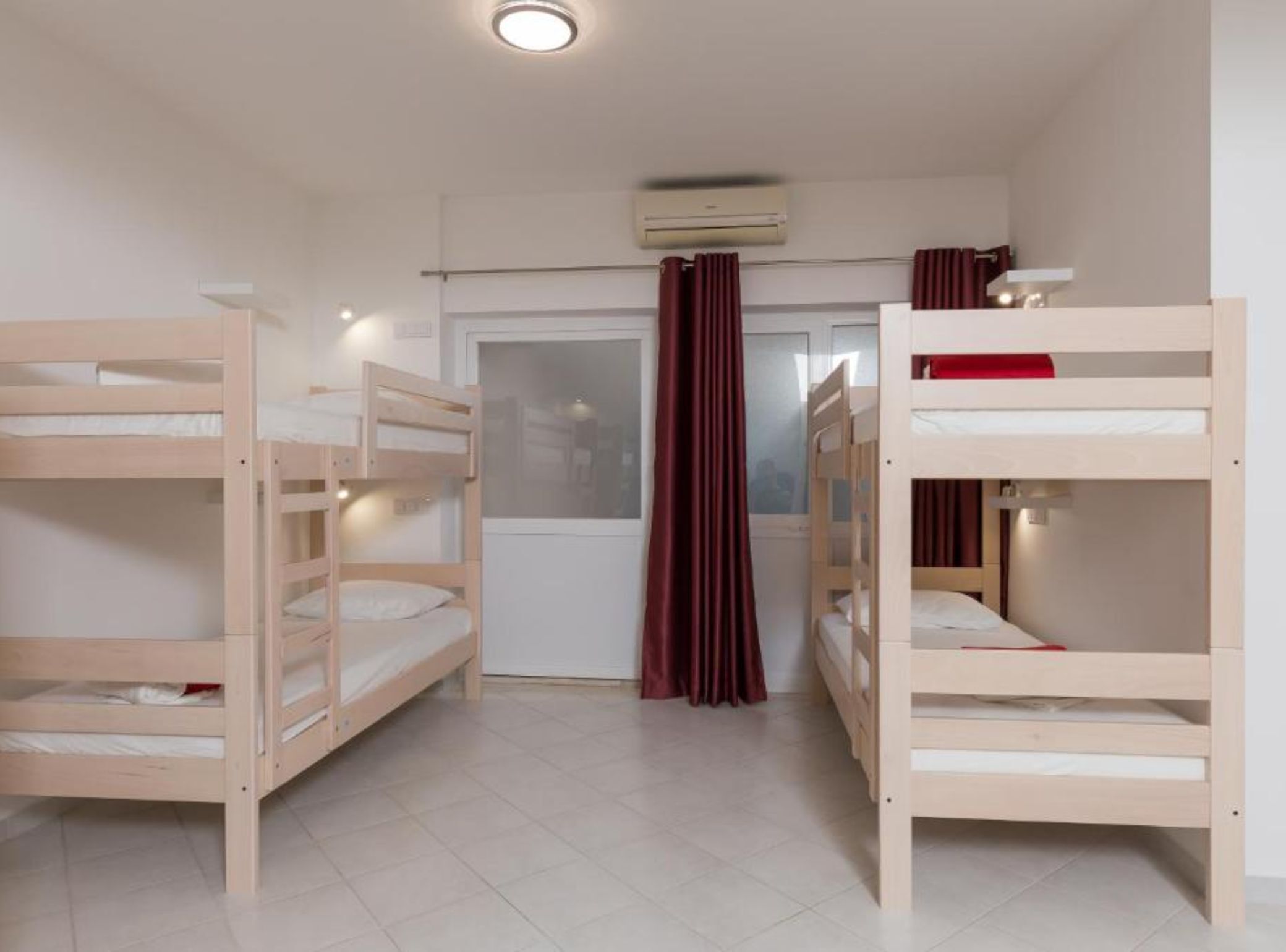 A room with three bunk beds, a window with curtains, and an air conditioning unit on the wall.