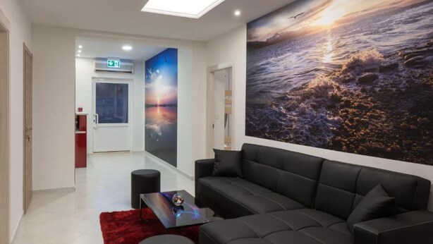 A modern lobby with a black leather sofa, a red rug, a glass coffee table, and a large ocean mural. - Hostel Free Bird (Dubrovnik)