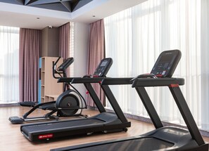 Une salle de sport moderne équipée de deux tapis de course, d’un vélo d’appartement et d’un banc de musculation.