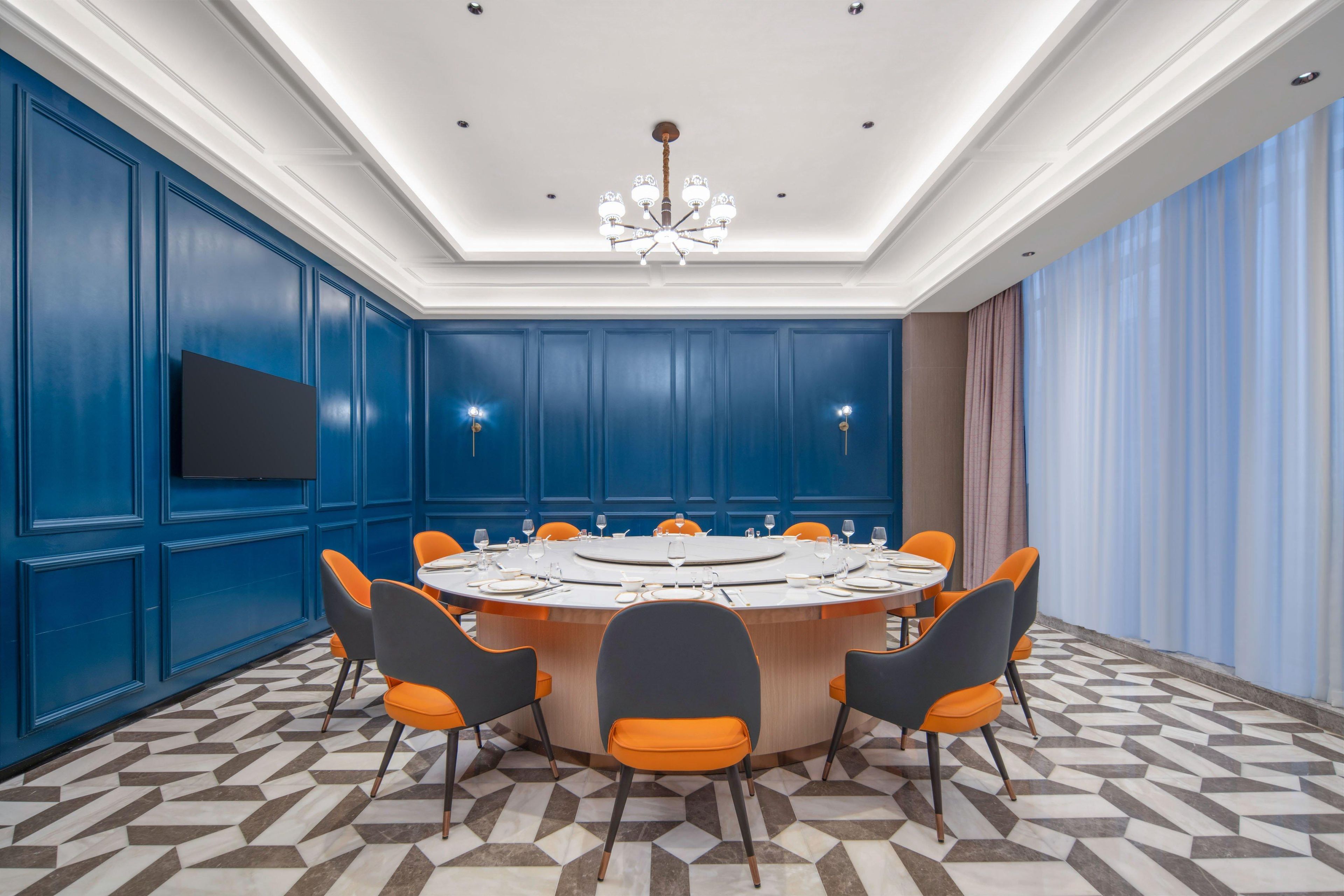 A conference room with a round table, orange and black chairs, a flat-screen TV, and blue paneled walls.