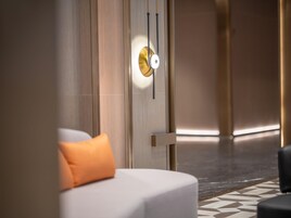 Una habitación de hotel moderna con diseño minimalista, que incluye una cama grande con un almohadón naranja, una lámpara fijada a la pared y un suelo con estampado.