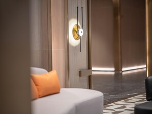 Une chambre d’hôtel moderne au design minimaliste, dotée d’un grand lit avec un oreiller orange, d’un luminaire fixé au mur et d’un sol à motifs.