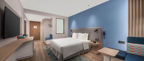 A modern hotel room with a large bed, a desk, a TV, and a seating area.