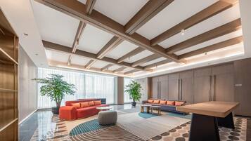 A modern lobby with a high ceiling, large windows, a seating area with sofas and a coffee table, and a reception desk.