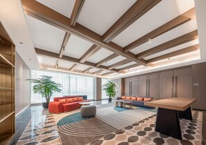 Un hall d’entrée moderne avec un plafond haut, de grandes fenêtres, un espace salon avec des canapés et une table basse, ainsi qu’un comptoir d’accueil.