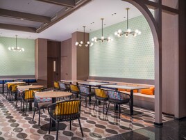 Un interior de restaurante moderno con mesas redondas, sillas negras y amarillas, y un suelo con diseño.