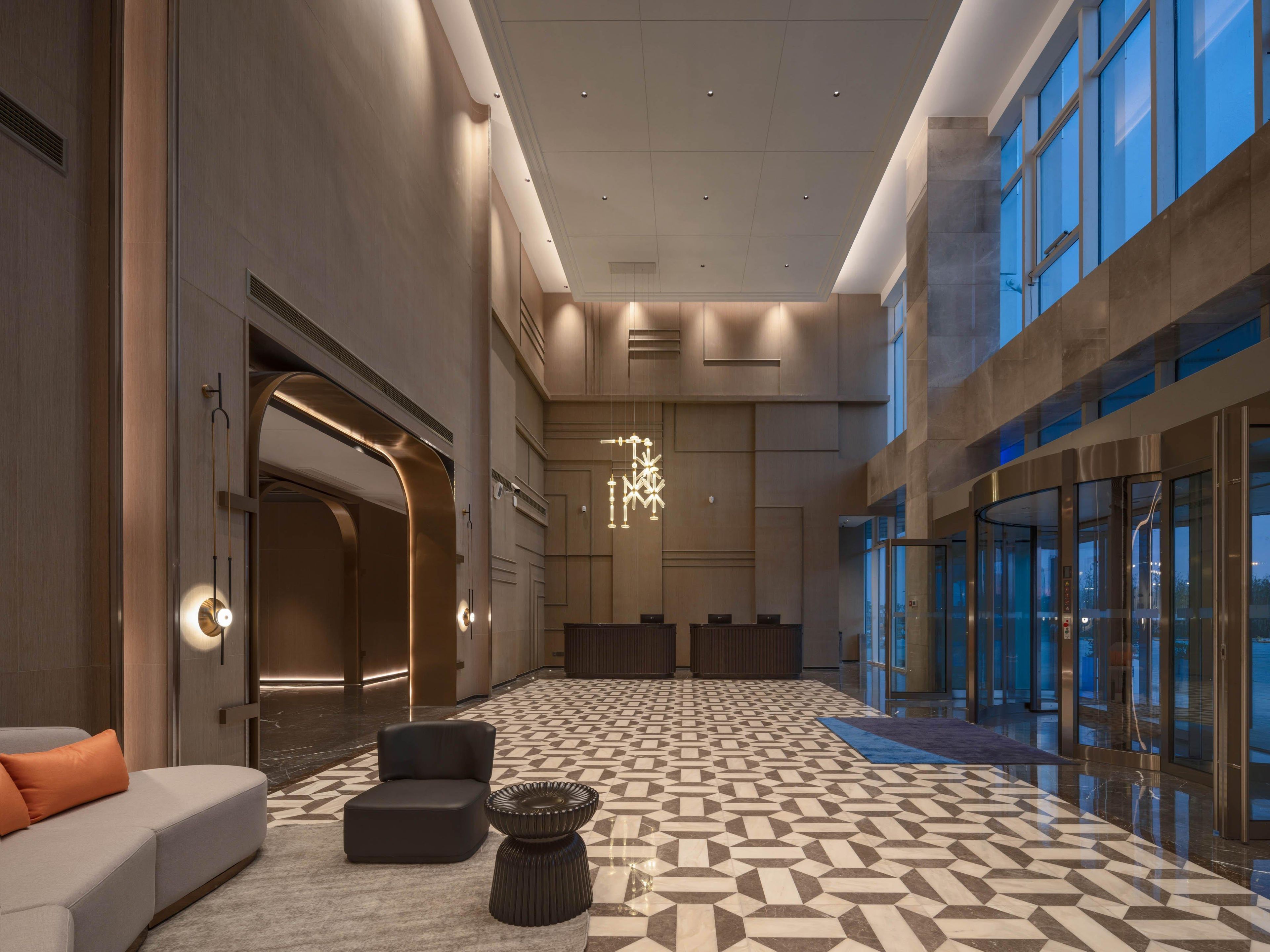 A spacious lobby with a geometric patterned floor, a modern chandelier, and a reception desk.