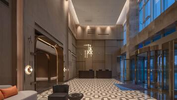 A spacious lobby with a geometric patterned floor, a modern chandelier, and a reception desk.