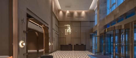 A spacious lobby with a geometric patterned floor, a modern chandelier, and a reception desk.