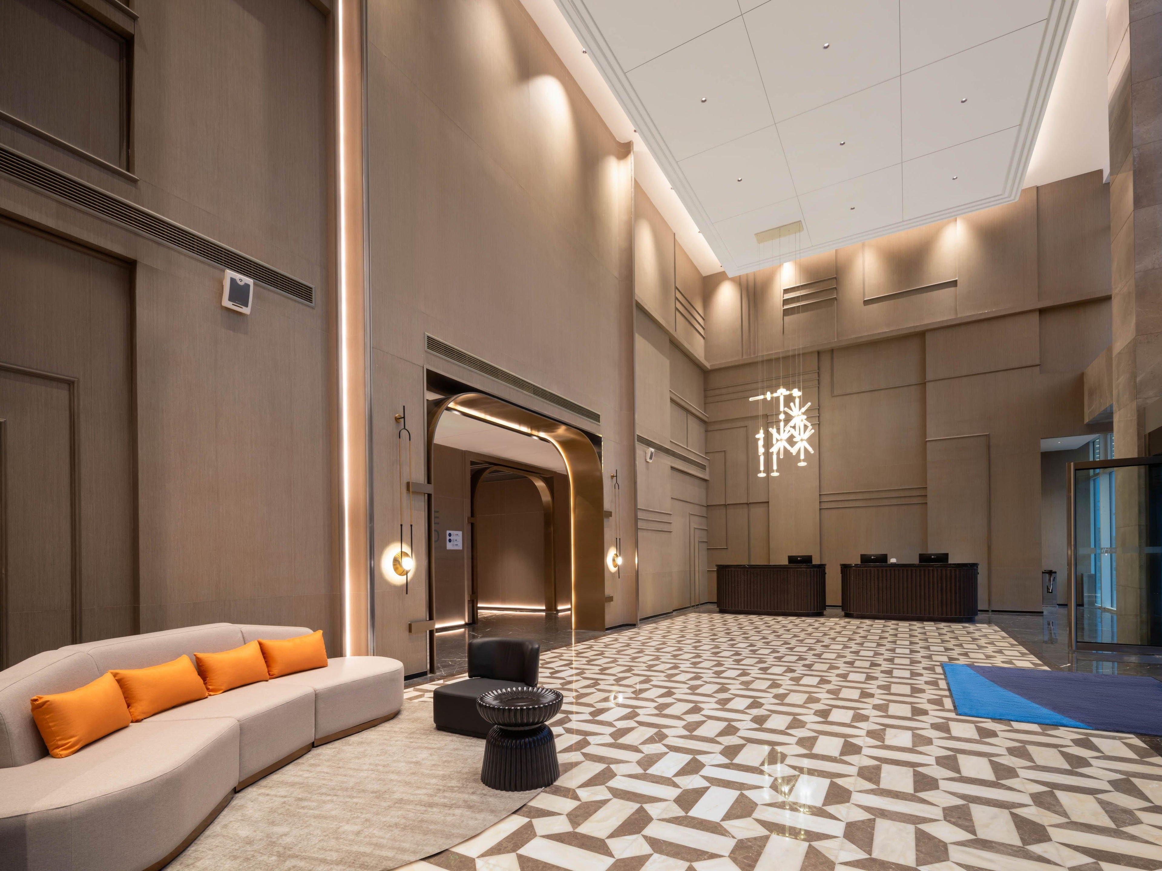 A spacious lobby with a patterned floor, a sofa with orange cushions, and a modern chandelier.