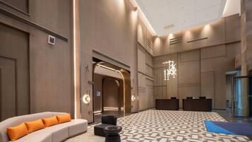 A spacious lobby with a patterned floor, a sofa with orange cushions, and a modern chandelier.