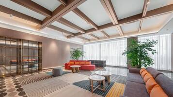 A modern living room with a high ceiling, large windows, and a mix of sofas and tables.