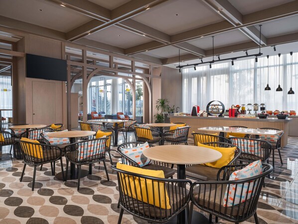 Un café moderne avec des tables rondes et des chaises noires, doté d’un sol à motifs et de grandes fenêtres.