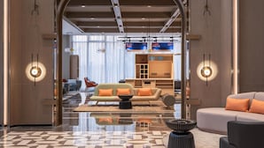 A modern hotel lobby with a geometric patterned floor, a central seating area with sofas and a coffee table, and a large arched doorway leading to a dining area with a bar. - Holiday Inn Express Taizhou Toumen Port (Taizhou)