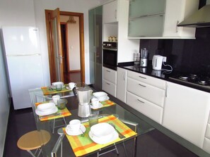 Una cocina moderna con una mesa de comedor preparada para cuatro personas, equipada con un refrigerador, horno y cafetera.