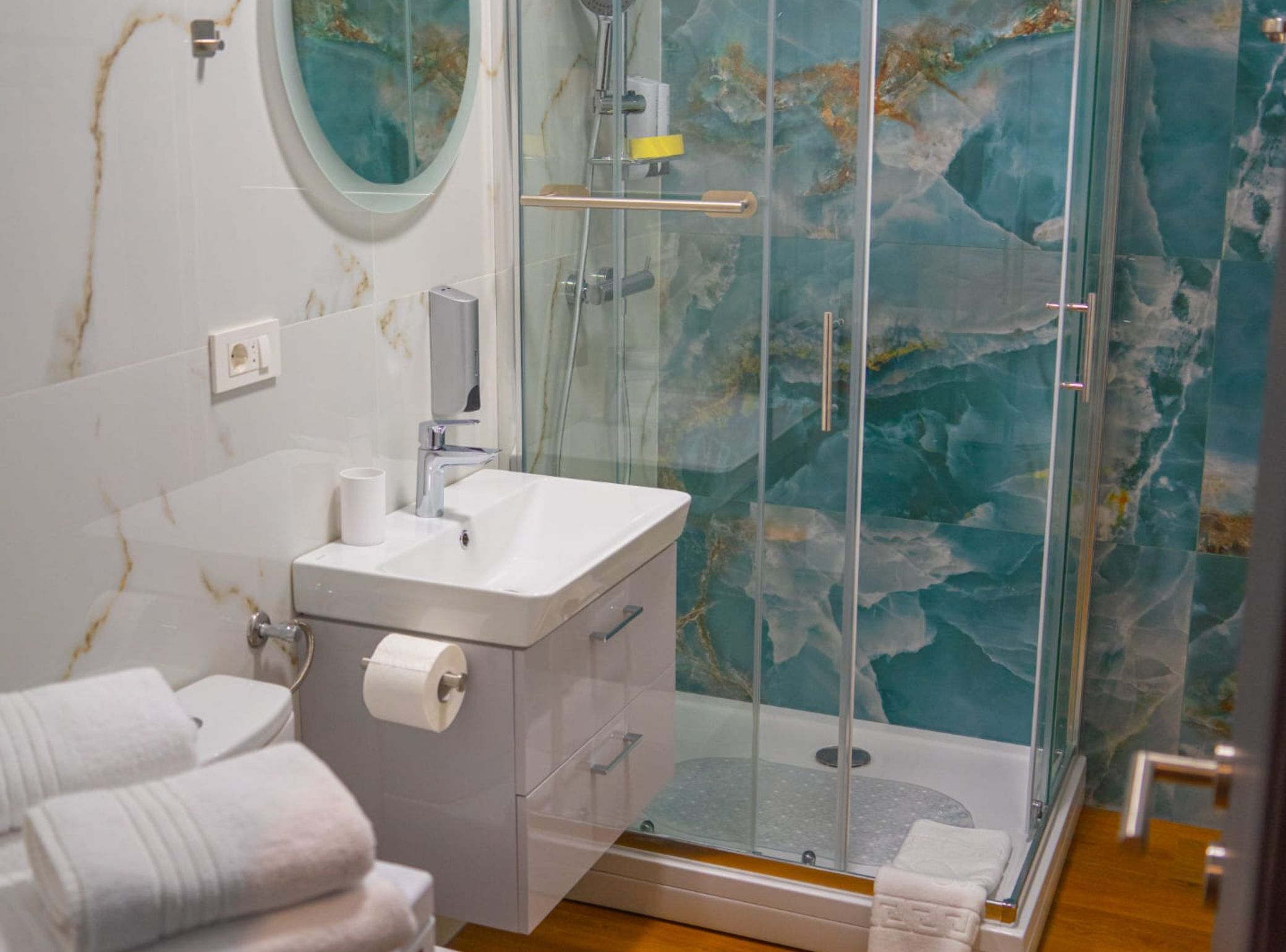 Un baño con ducha envuelta en vidrio, un lavamanos con encimera de mármol y un perchero con toallas.