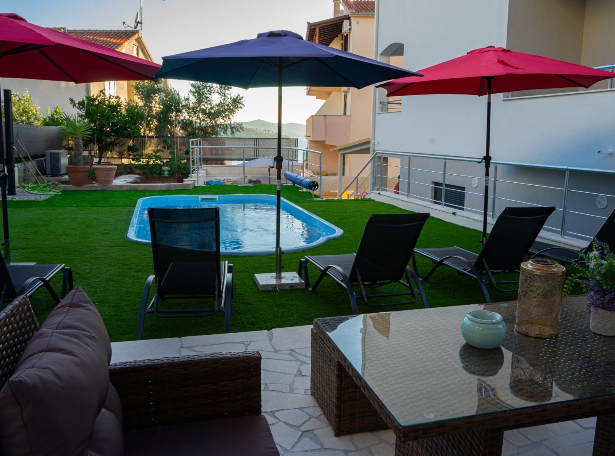 A rooftop pool area with a glass table, lounge chairs, and umbrellas.