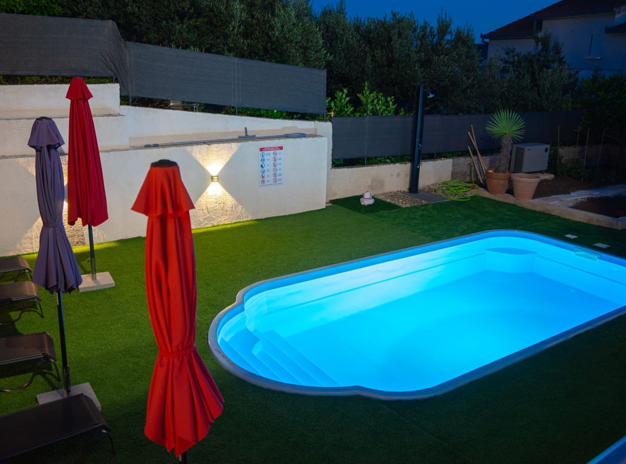 A swimming pool with artificial grass, red umbrellas, and a white wall with a sign.