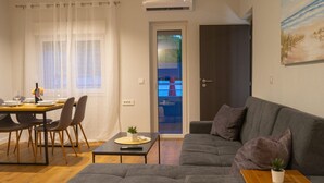 A modern living room with a grey sofa, a dining table with chairs, and a small table with a plant. - Apartments Neli (Okrug)