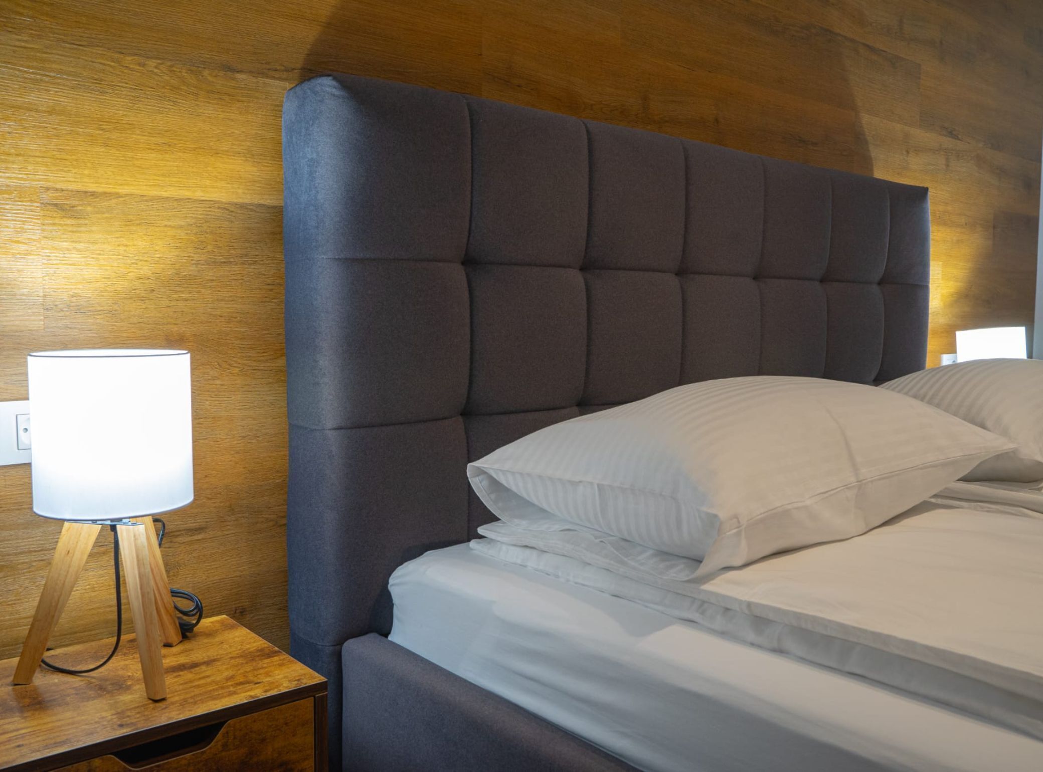 A neatly made bed with a tufted headboard, a bedside lamp, and a wooden nightstand.