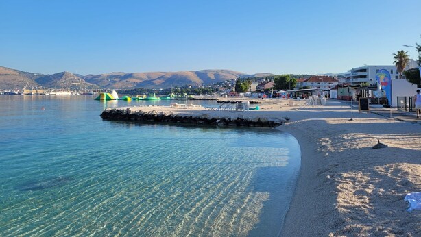 A coastal beach with clear waters, a sandy shore, and a small pier with inflatable structures. - Apartments Neli (Okrug)
