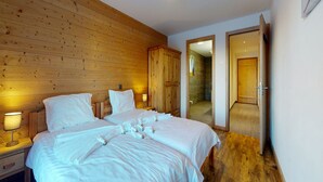 A bedroom with two beds, wooden walls, a wooden floor, and a bathroom visible through an open door.