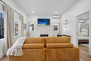 A modern living room with a sofa set, a fireplace, a TV, and a large window with curtains.