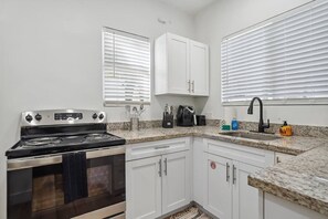Una cocina con armarios blancos, estufa y pileta.