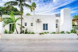 Un edificio moderno blanco con dos unidades de aire acondicionado, una ventana pequeña y una base de hormigón.