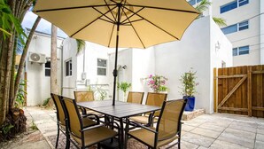 A patio with a table and chairs under a large umbrella, surrounded by potted plants and a wooden fence. - Casa Roselle full 2/2 (Hollywood)