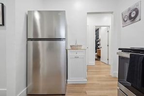 Una cocina con un refrigerador de acero inoxidable, un armario blanco y suelo de madera.