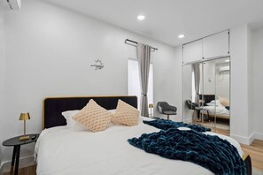 A modern bedroom with a bed, bedside tables, a mirror, and a wardrobe.