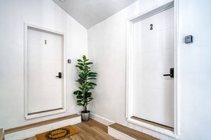 Un pasillo con dos puertas blancas, cada una con un número. Una planta en maceta se encuentra entre las puertas.