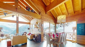 A spacious living area with a wooden ceiling, large windows offering mountain views, a dining area with a table set for six, and a cozy seating area with a sofa and chairs. - Etoiles des Neiges Luxe & Jacuzzi Chalet (Heremence)