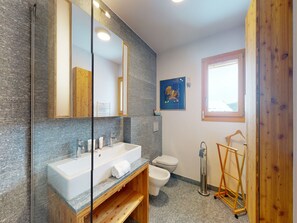 Een moderne badkamer met een grote spiegel, een witte wastafel, een toilet en een douchehoek.