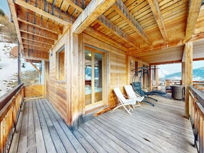 Una cabaña de madera con un porche, una puerta de vidrio que da al interior y vistas del paisaje nevado.