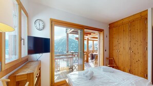 A bedroom with a bed, a TV, a wooden desk, and a view of mountains through a sliding door. - Etoiles des Neiges Luxe & Jacuzzi Chalet (Heremence)