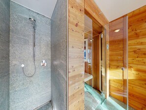 Un baño moderno con ducha, una pared de madera y un cerramiento de vidrio que da a un pasillo.