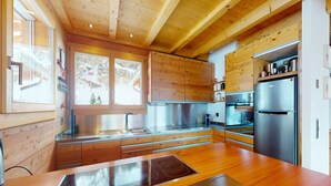 A modern kitchen with wooden cabinets, stainless steel appliances, and a large island with a built-in stovetop. - Etoiles des Neiges Luxe & Jacuzzi Chalet (Heremence)