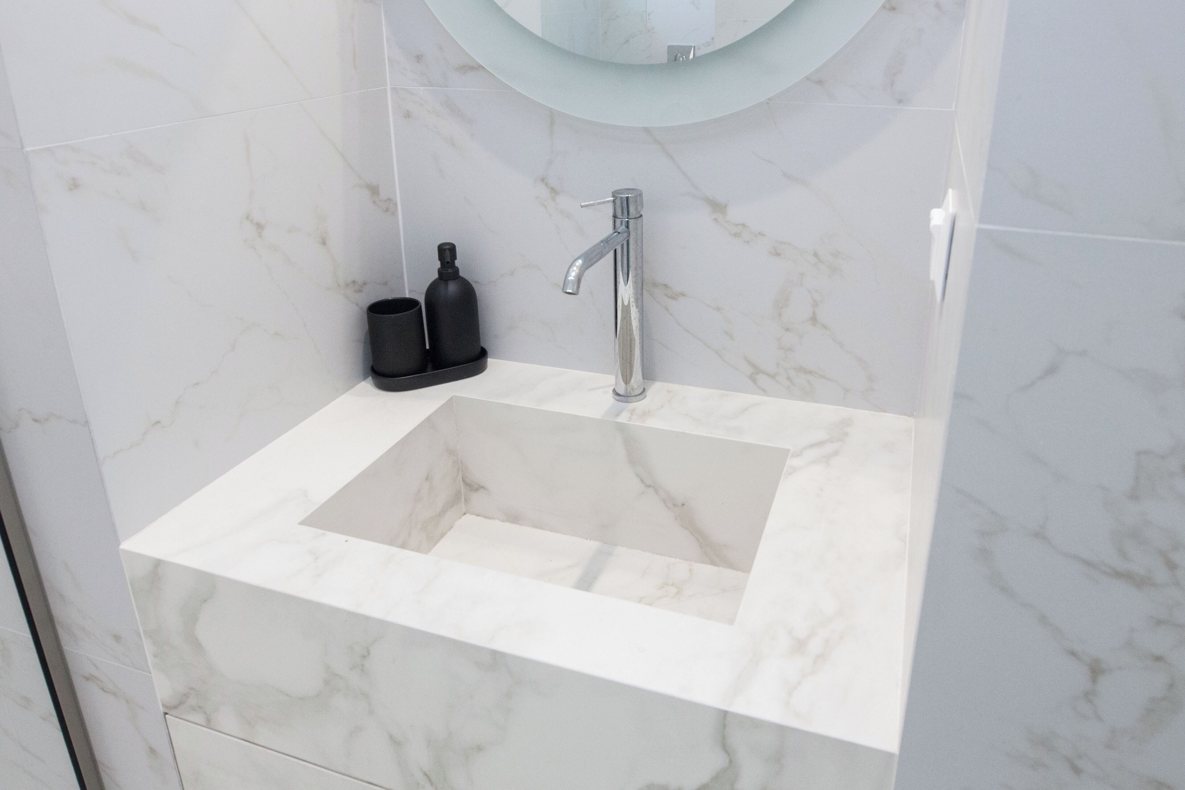 A bathroom with a marble sink, a modern faucet, and a round mirror above it.