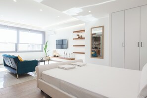 A modern bedroom with a large bed, a blue sofa, a desk, and a wardrobe. - Stylish Modern Suite at Piraeus Port (Piraeus)