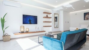 A modern living room with a blue sofa, a flat-screen TV, wooden shelves, and a large mirror. - Stylish Modern Suite at Piraeus Port (Piraeus)