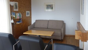 A cozy room with a sofa, a small table, and a bookshelf. - Pleasant Apartment With Balcony (Veysonnaz)