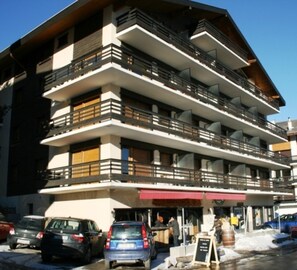 A multi-story building with balconies, a ground-level restaurant, and cars parked in front. - Pleasant Apartment With Balcony (Veysonnaz)