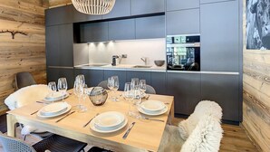 A modern dining area with a wooden table set for a meal, a hanging light fixture, and built-in kitchen cabinets. - Lovely Apartment Near ski Lift (Anniviers)