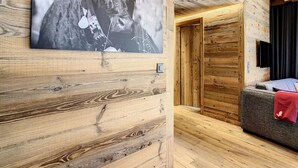 A wooden cabin interior with a large framed photograph on the wall, a television mounted on the wall, and a cozy seating area with a red blanket. - Lovely Apartment Near ski Lift (Anniviers)