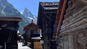 A narrow street lined with traditional wooden buildings, a wooden gate, and a mountain peak in the background. - Lovely Apartment Near ski Lift (Anniviers)