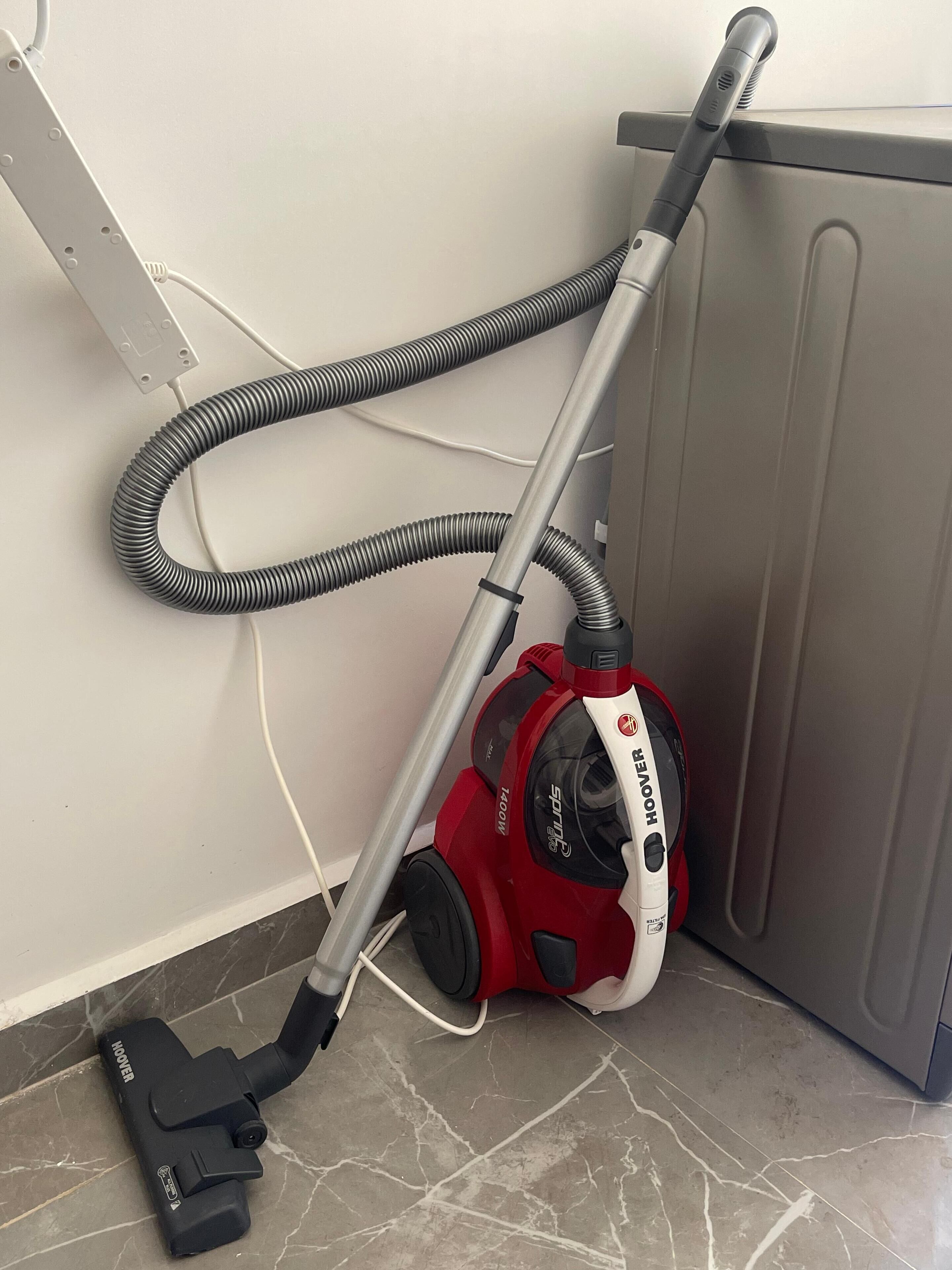 A vacuum cleaner with a hose and a power cord plugged into a wall socket.