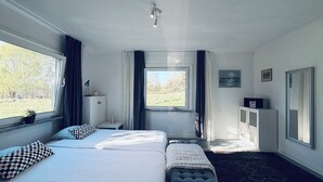 Ett hotellrum med en säng, ett skrivbord, ett fönster med utsikt över träd, ett skåp och en spegel.